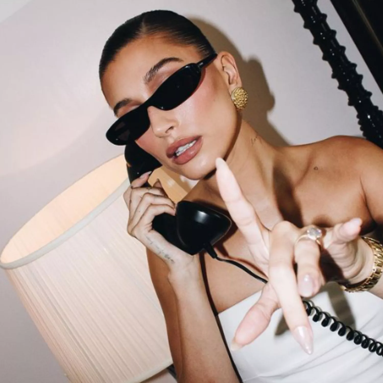 Hailey Bieber on the phone holding up one hand with a velvet pink manicure.