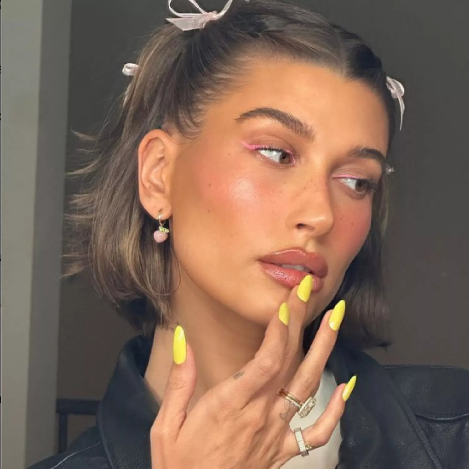 Hailey Bieber taking a selfie wearing pink eyeliner and yellow nails.