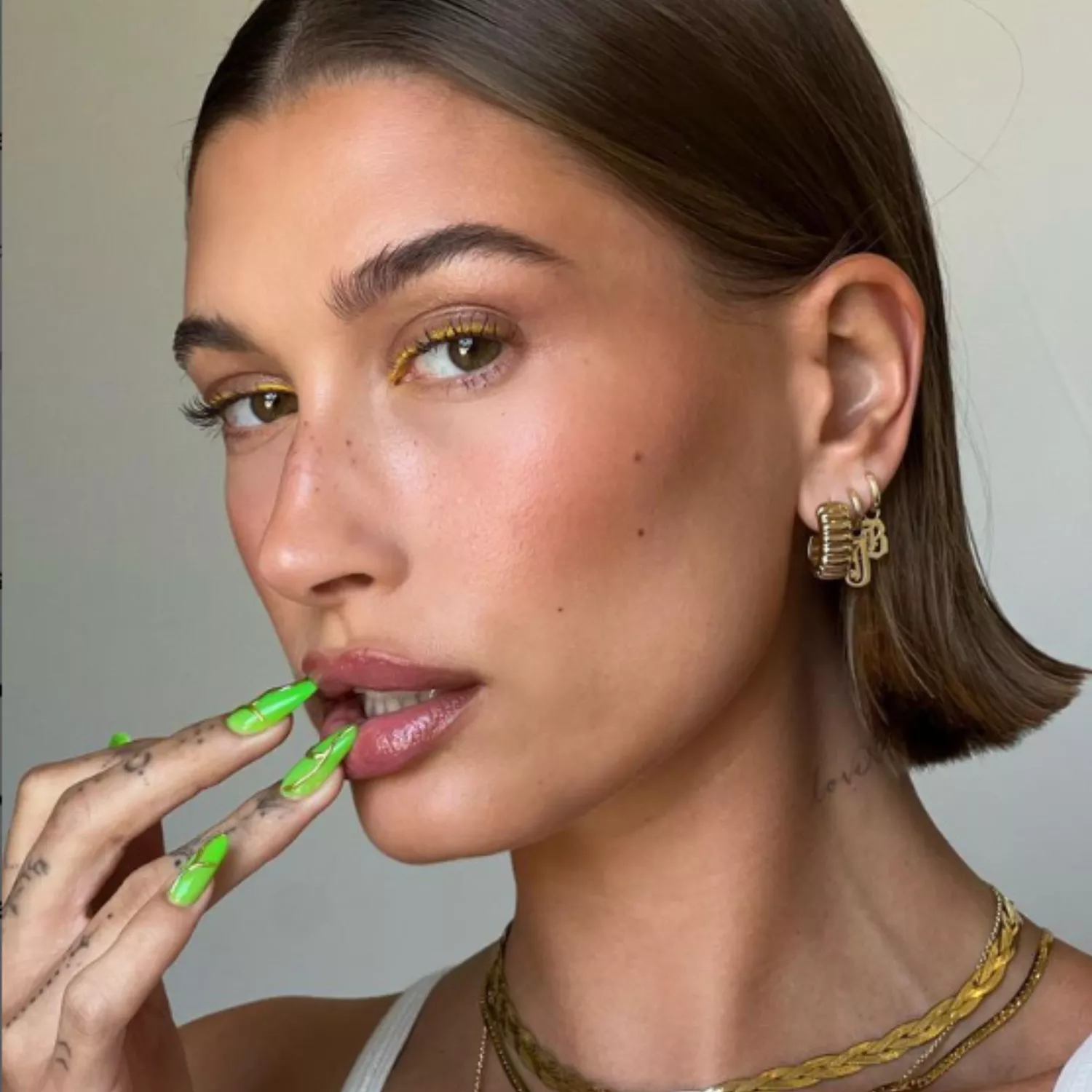 Hailey Bieber wearing yellow eyeliner and molten metal nails with a neon green base.