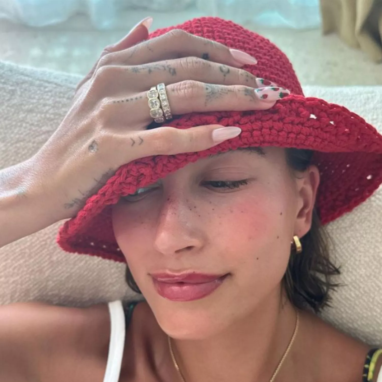 Hailey Bieber in a red crochet hat and neutral nails with a strawberry decals on two accent nails.