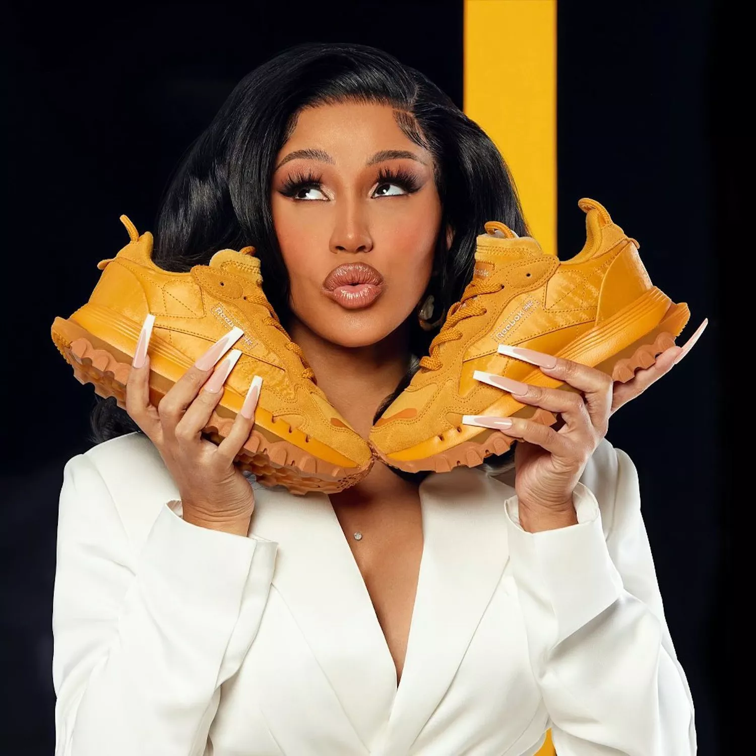 Close up of Cardi B with two gold sneakers and long French tips