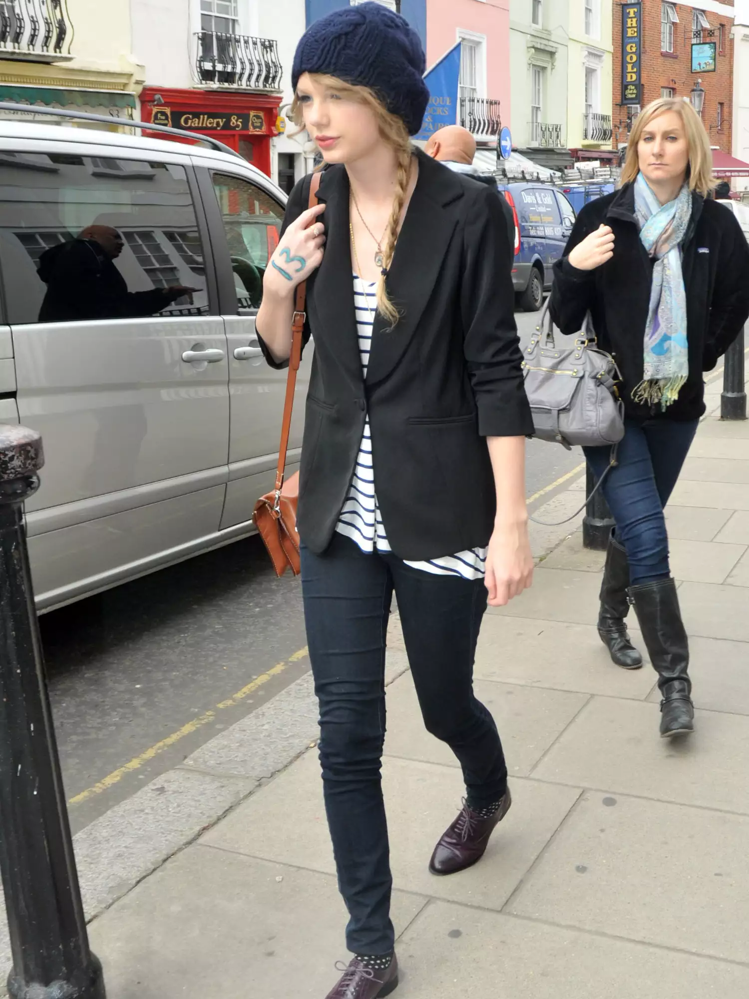 Taylor Swift wearing a black blazer, black-and-white striped shirt, blue beanie, and brown leather bag while shopping in London