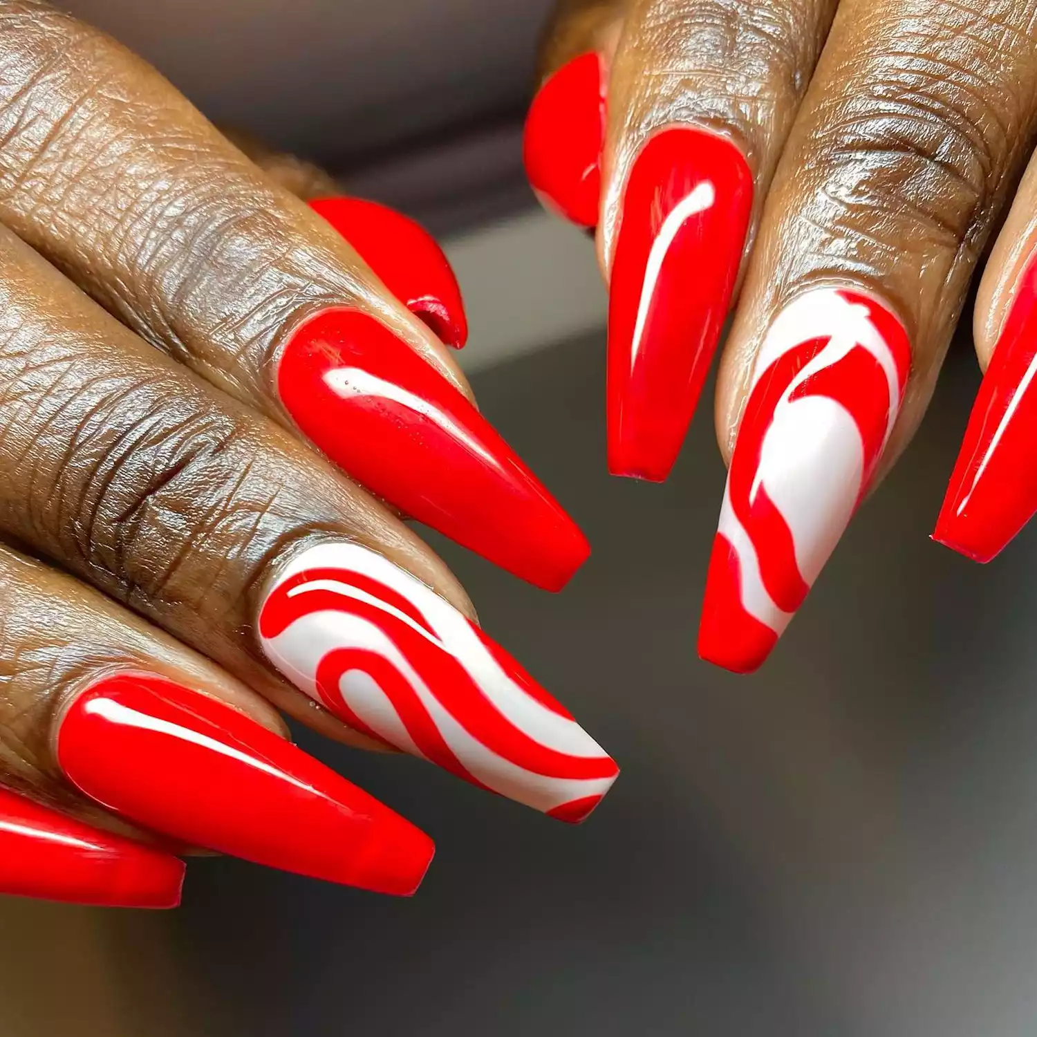 Close up of a manicure with solid red and red swirl nails