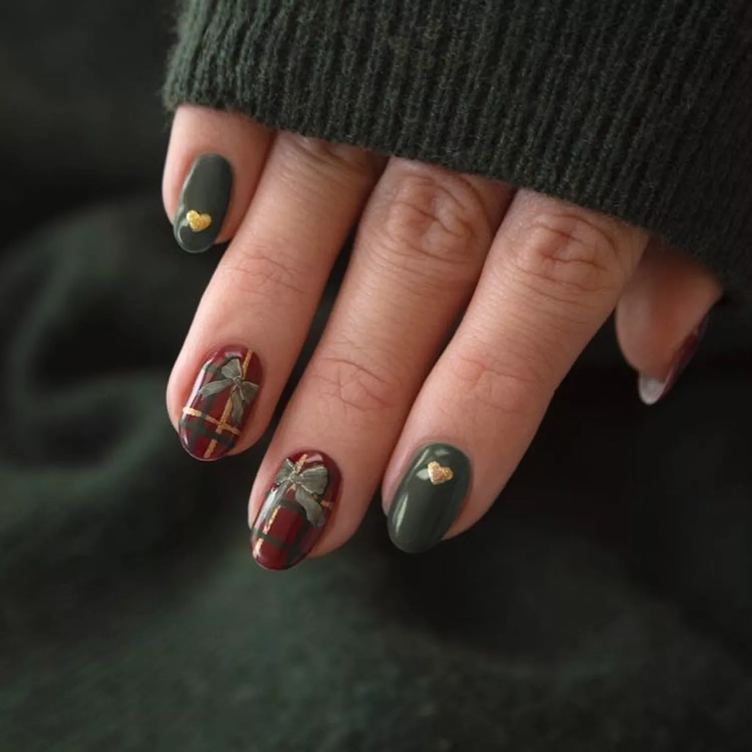 Close up of a manicure with green nails with gold hearts and plaid nails with green bows