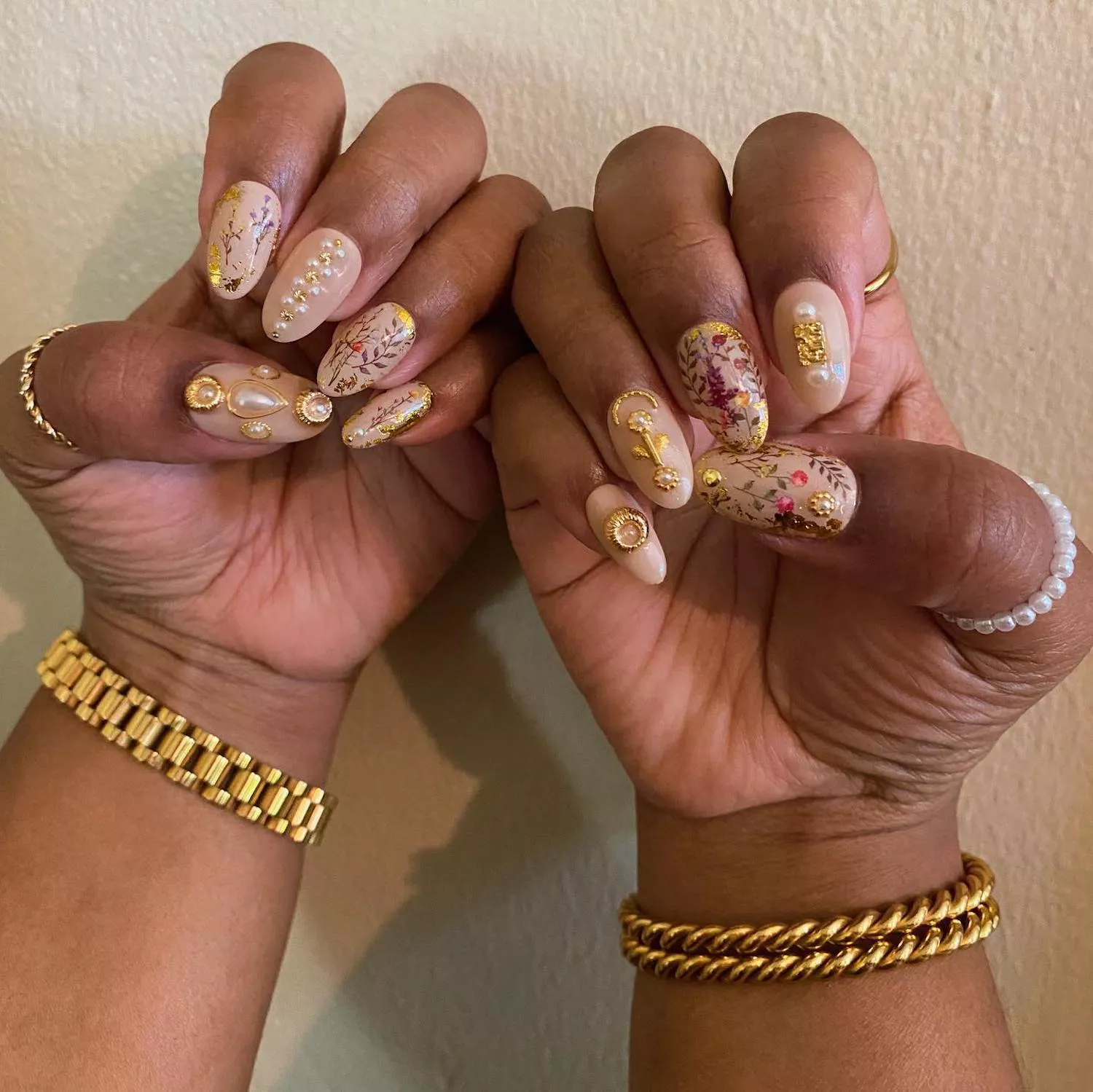 Manicure with nude base, botanical nail designs, and pearl and golden jewelry accents