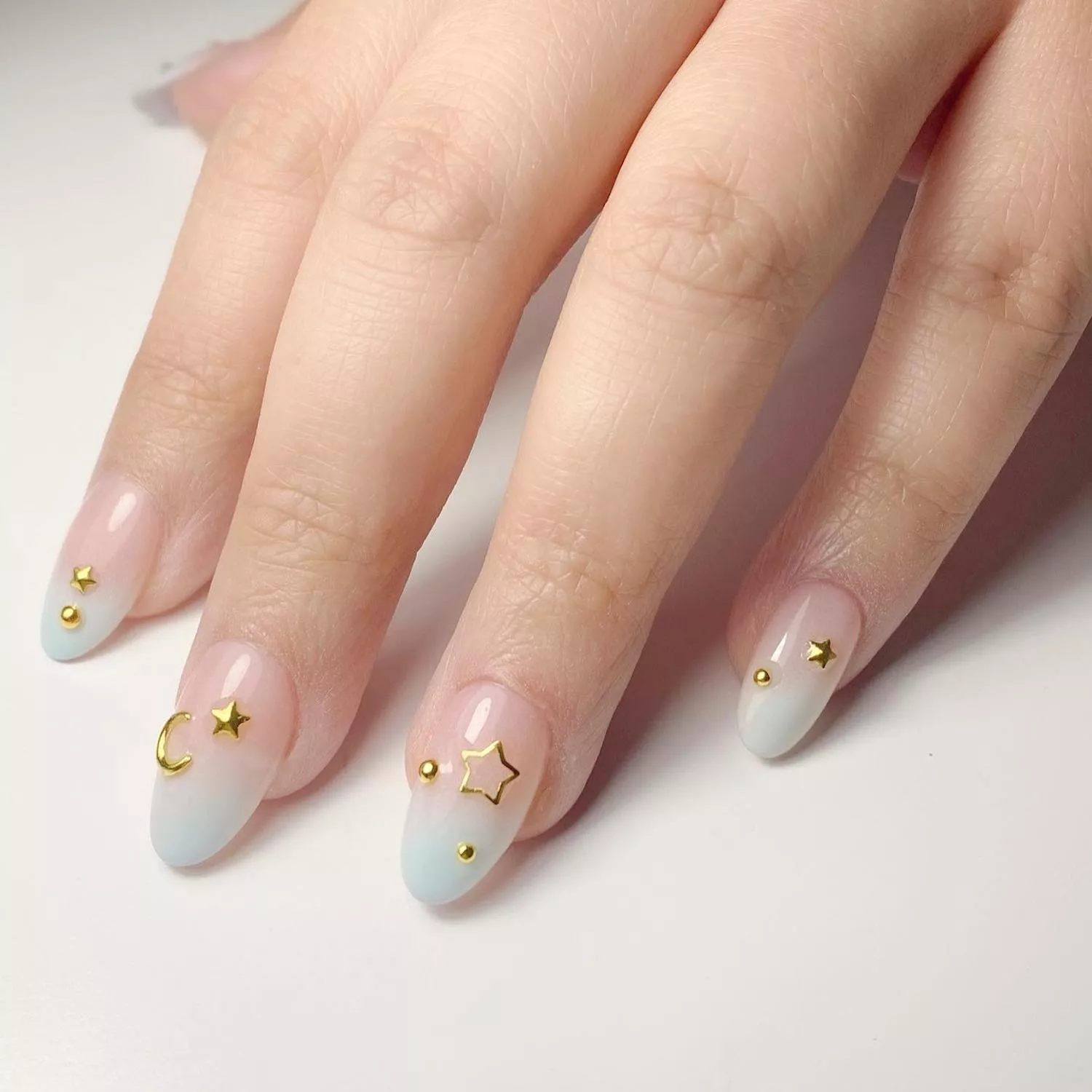 Pastel pink-to-blue ombre manicure with gold star, moon, and dot decals