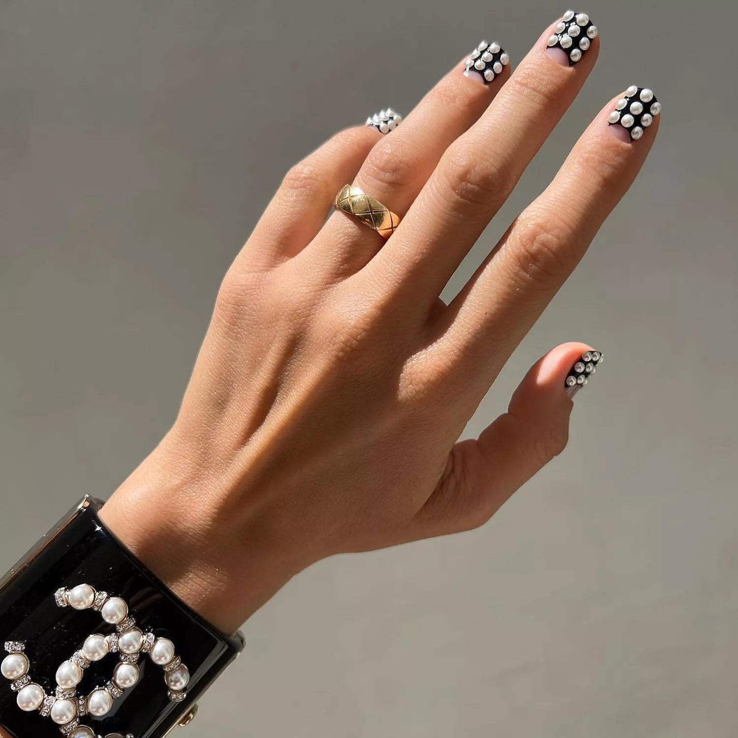 Manicure with black base, negative space half-moons, and 3D pearl accents with gold ring and Chanel pearl bracelet