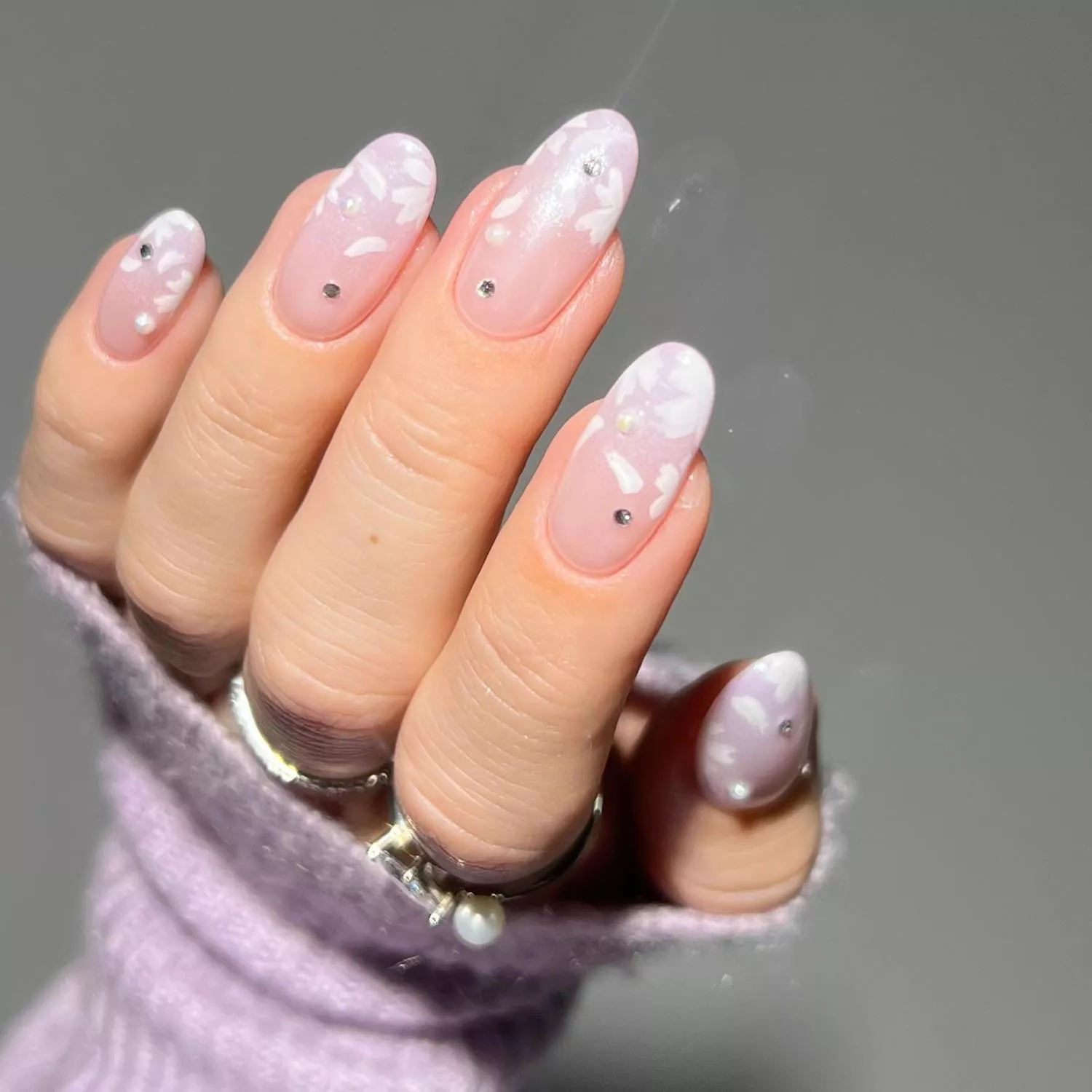 Pale pink chrome manicure with white flower petal designs and rhinestones