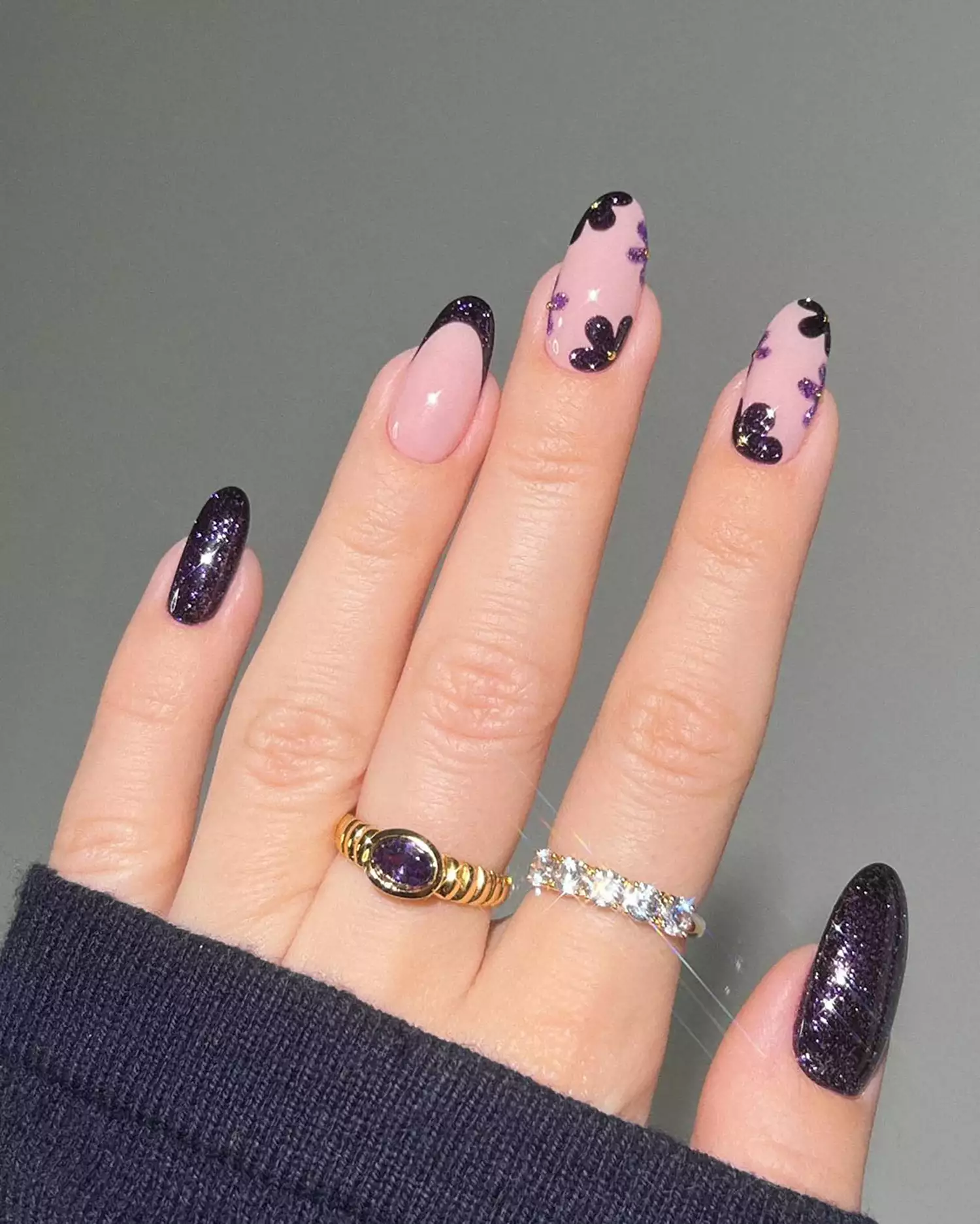 Close up of a manicure with dark purple glitter accent nails, French tips, and floral details