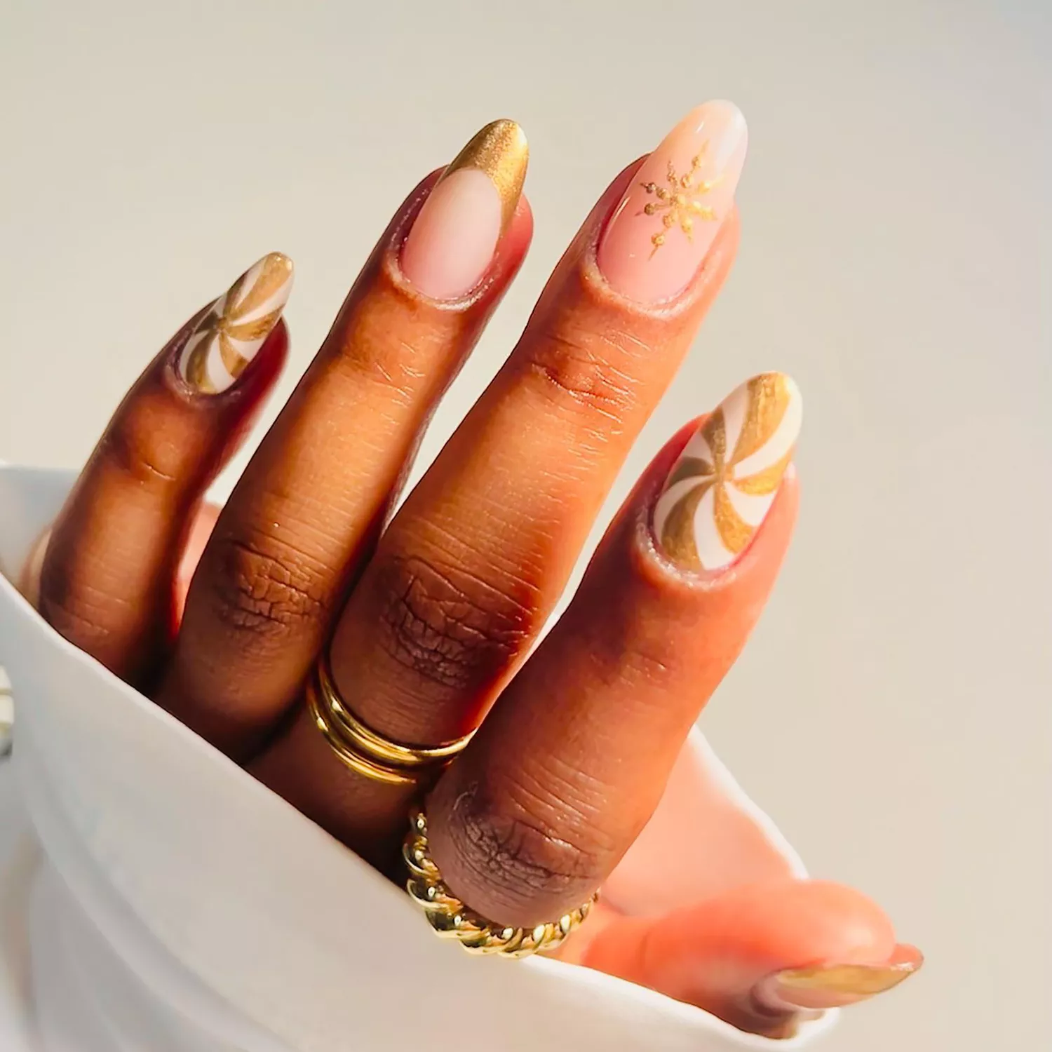 Close up of a manicure with gold peppermint swirls, French tips, and snowflakes