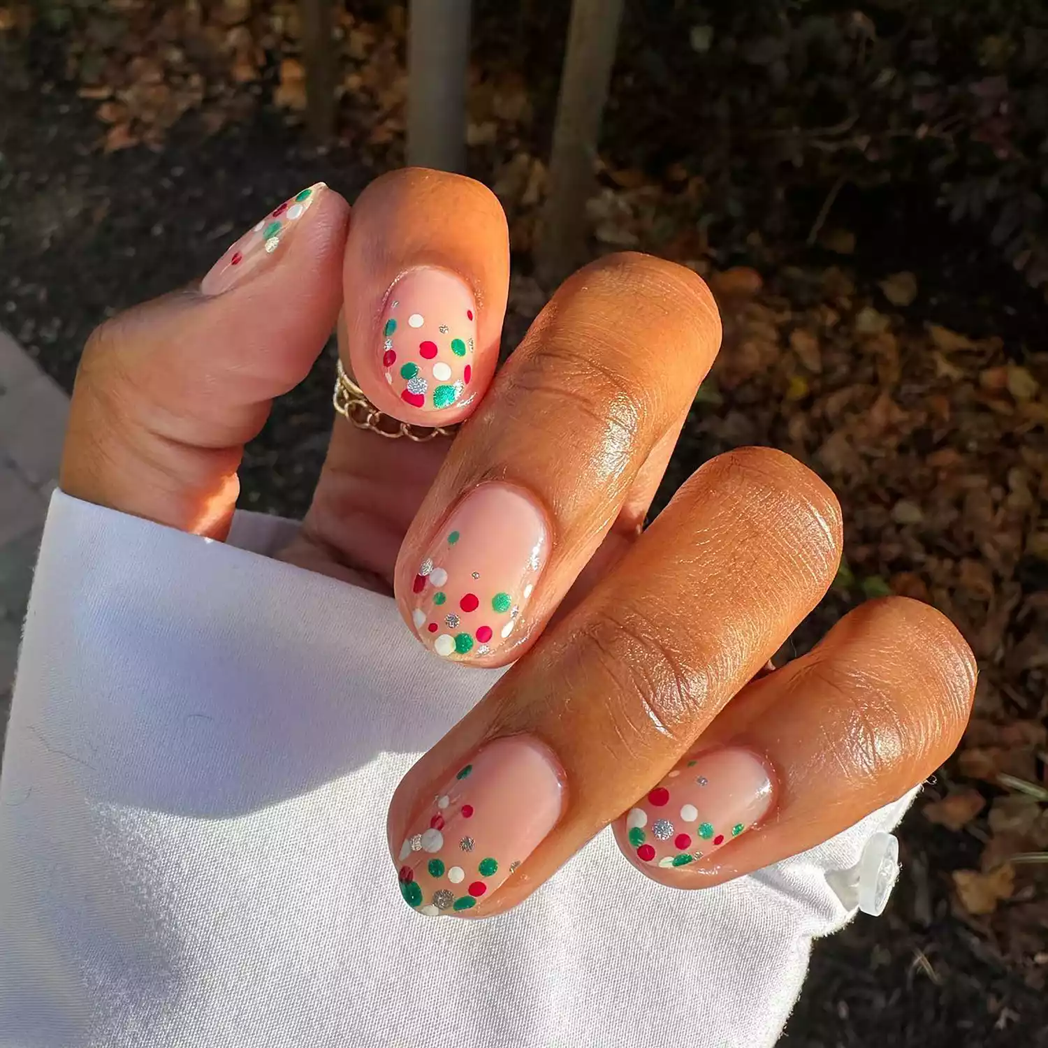 Close up of a neutral-base manicure with white, green, red, and silver polka dots at the tips