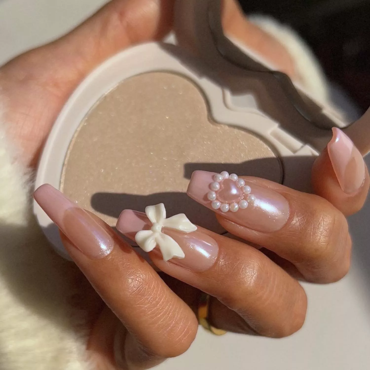 Manicure with pearlescent pink base and 3D pearl, heart, and bow accents