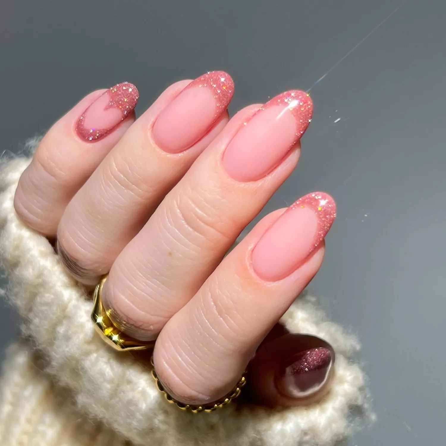 Close up of a glittery pink French manicure with a heart accent nail