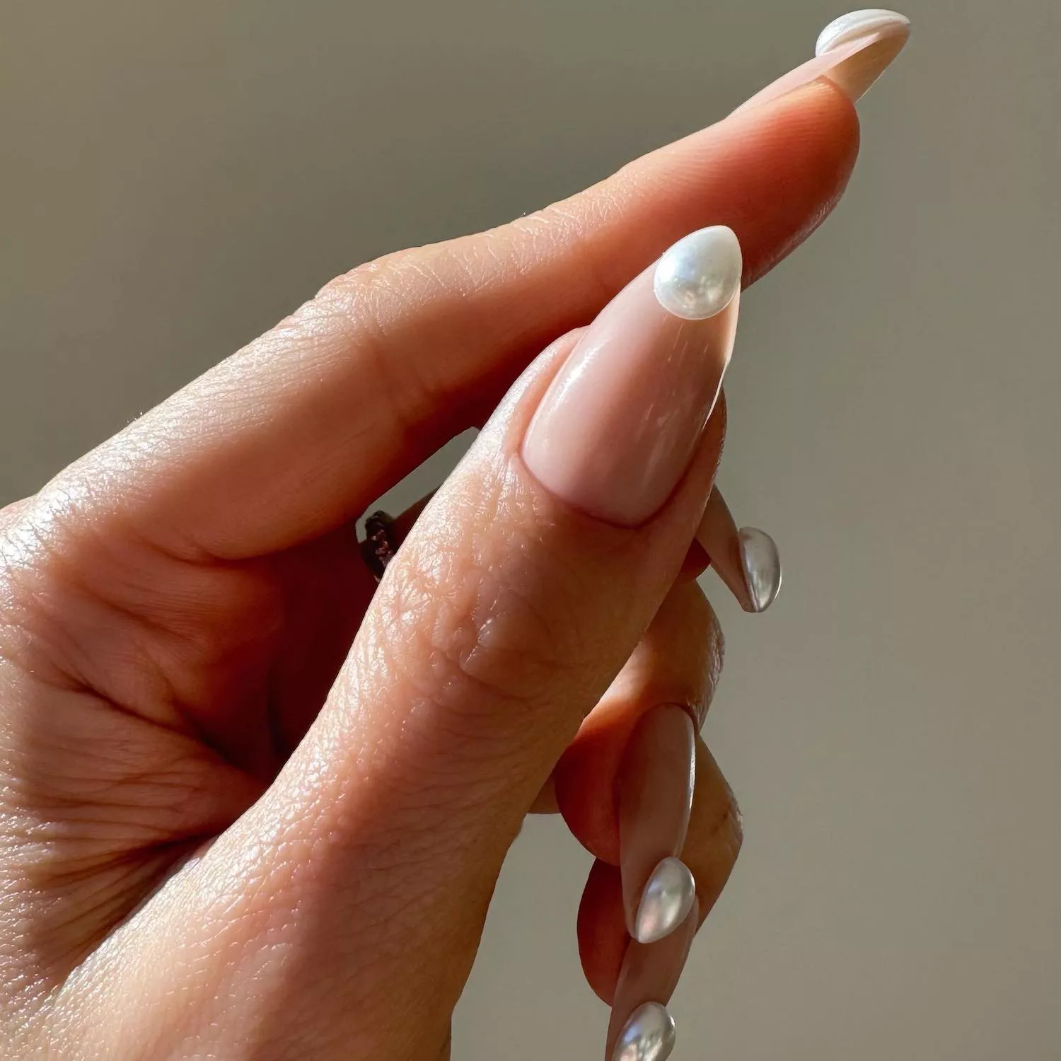 Neutral extended almond-shaped nails with pear-shaped pearl accents at tip