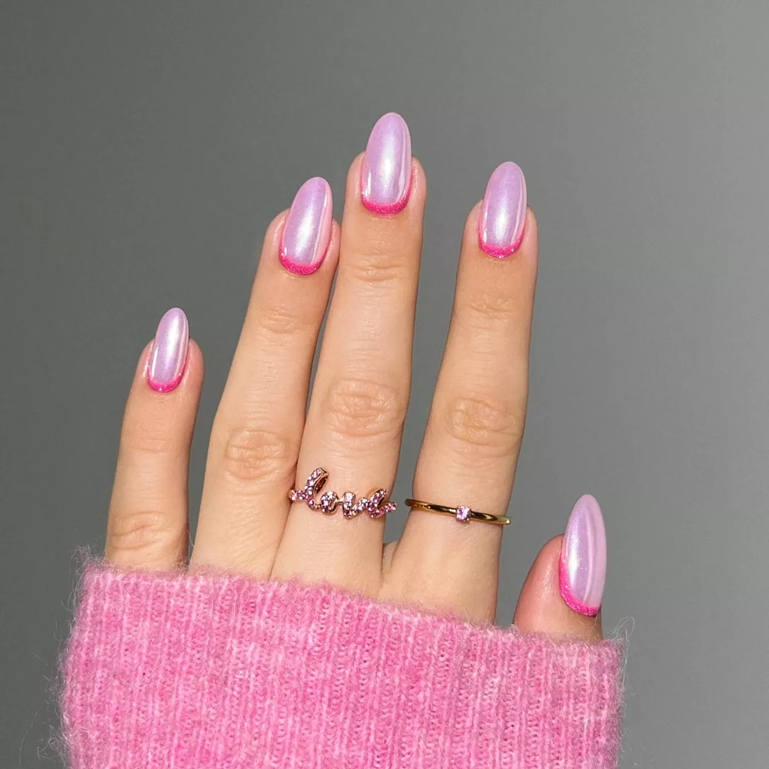 A hand with a pink chrome manicure, glittery pink at the cuticles