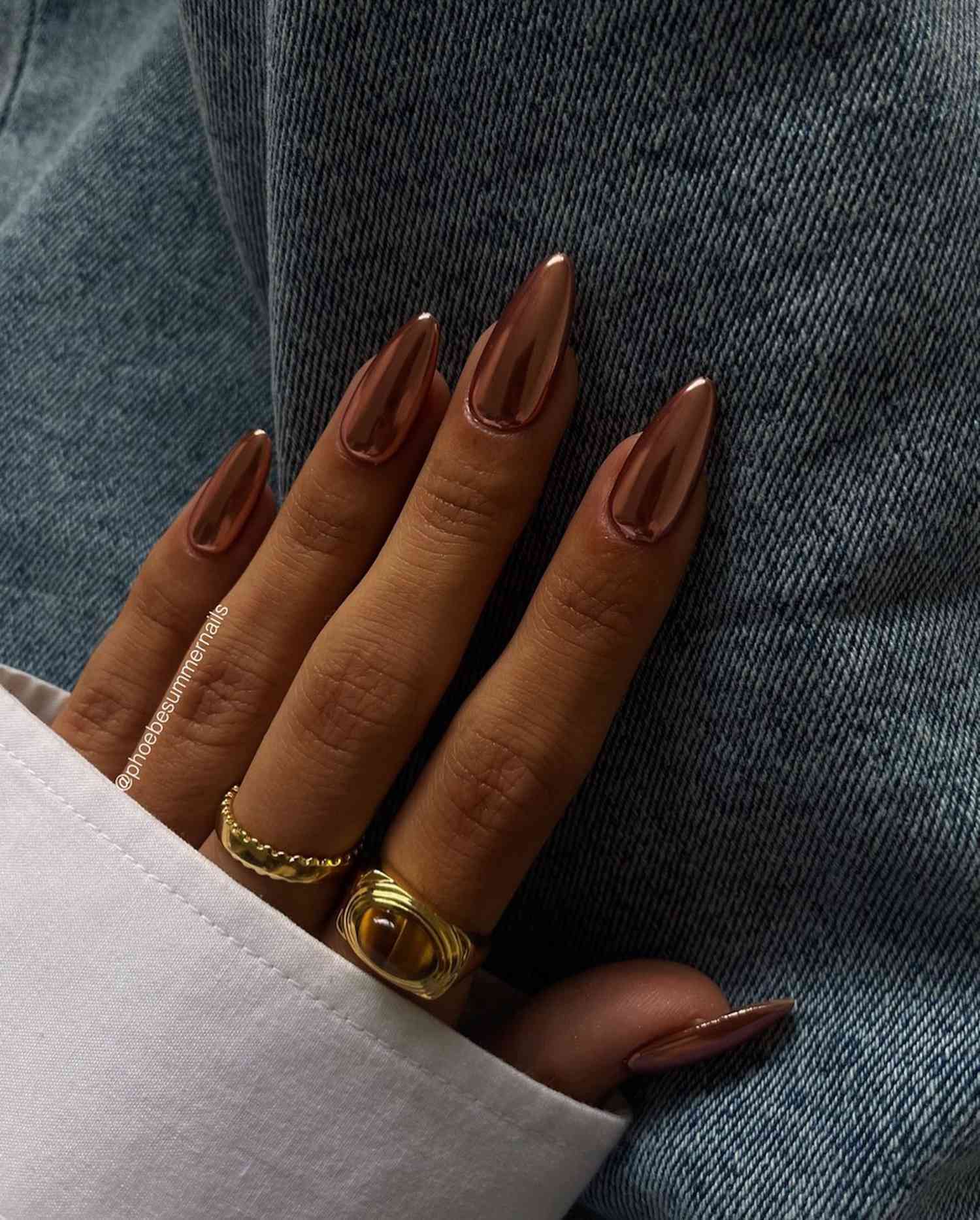 A hand with a brown chrome manicure resting against a pair of jeans