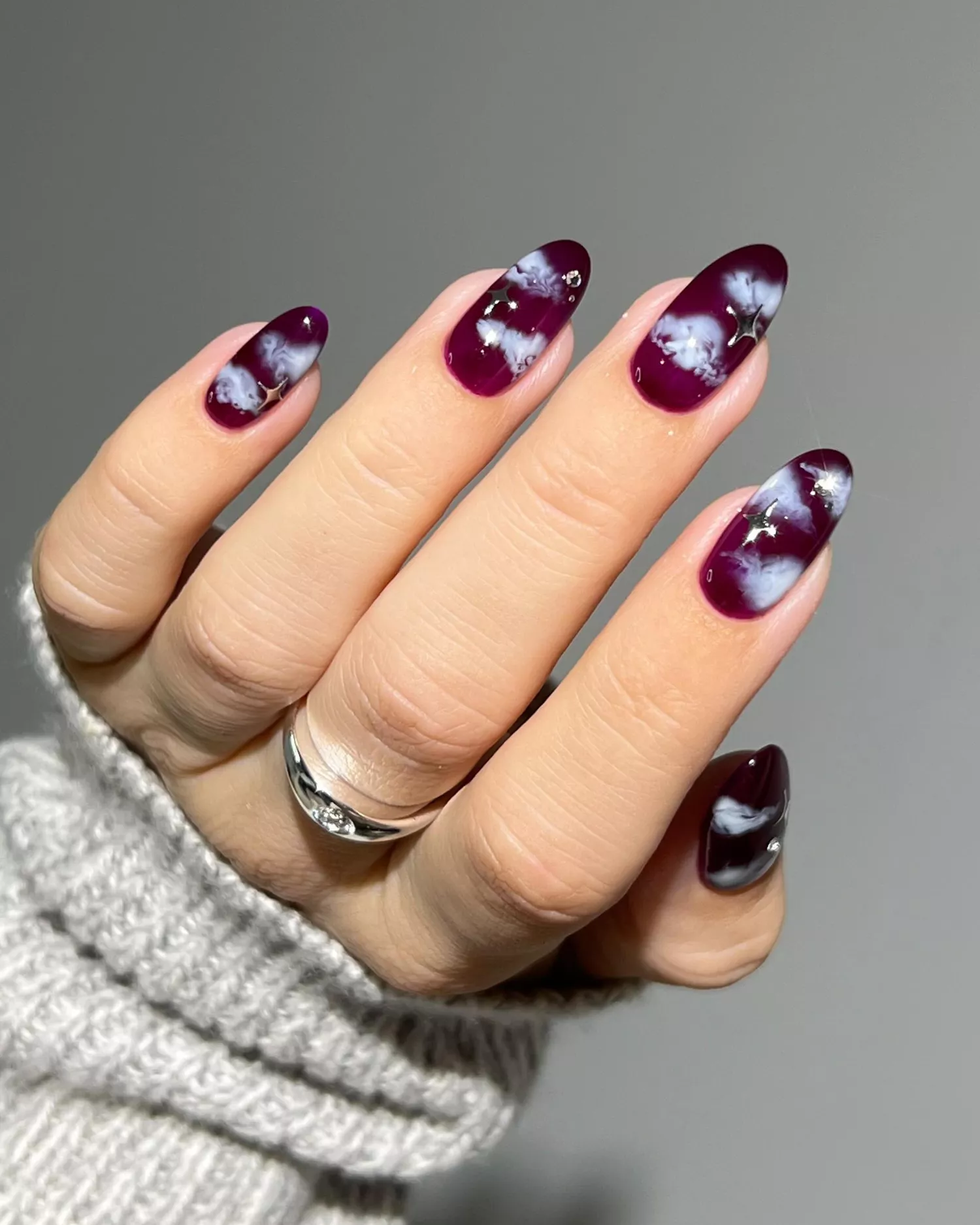 Close up of a Bordeaux-colored manicure with cloud and silver star accents