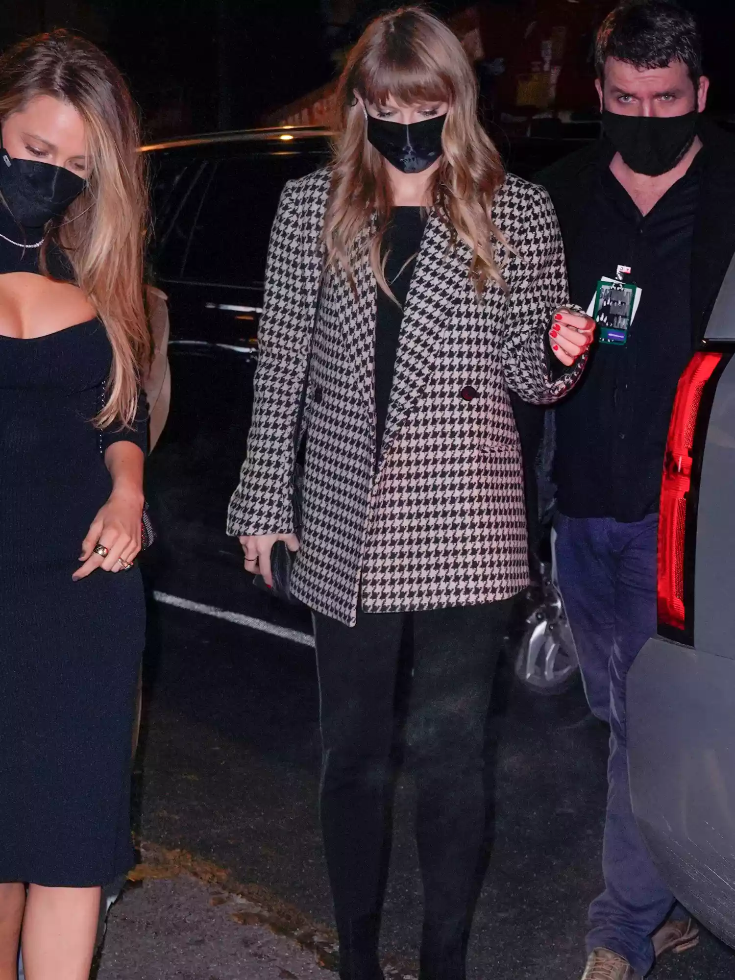 Taylor Swift wearing black pants, houndstooth blazer, and black face mask while walking with Blake Lively