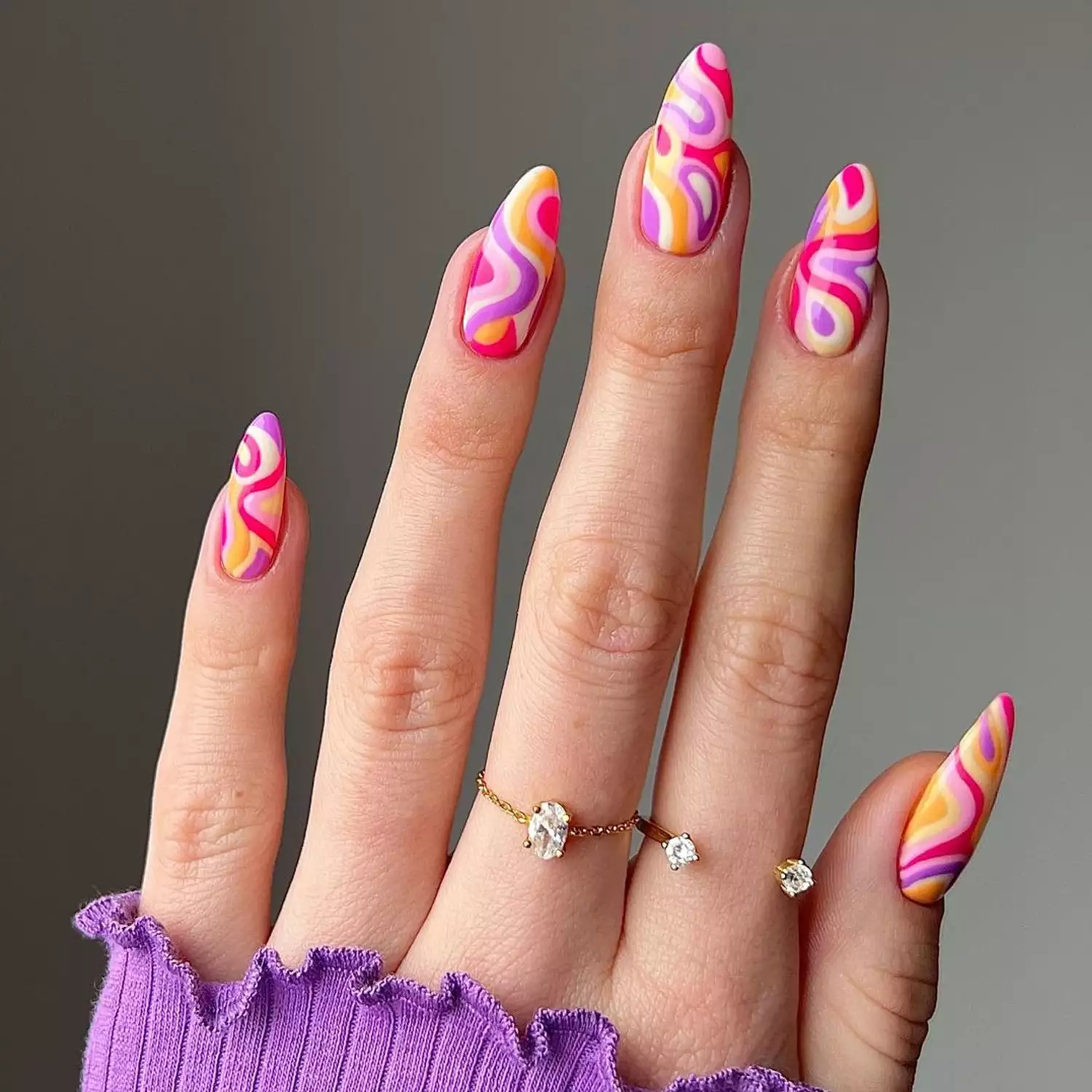 Barbie Swirl Nails in shades of pink, purple, yellow and white against a gray wall