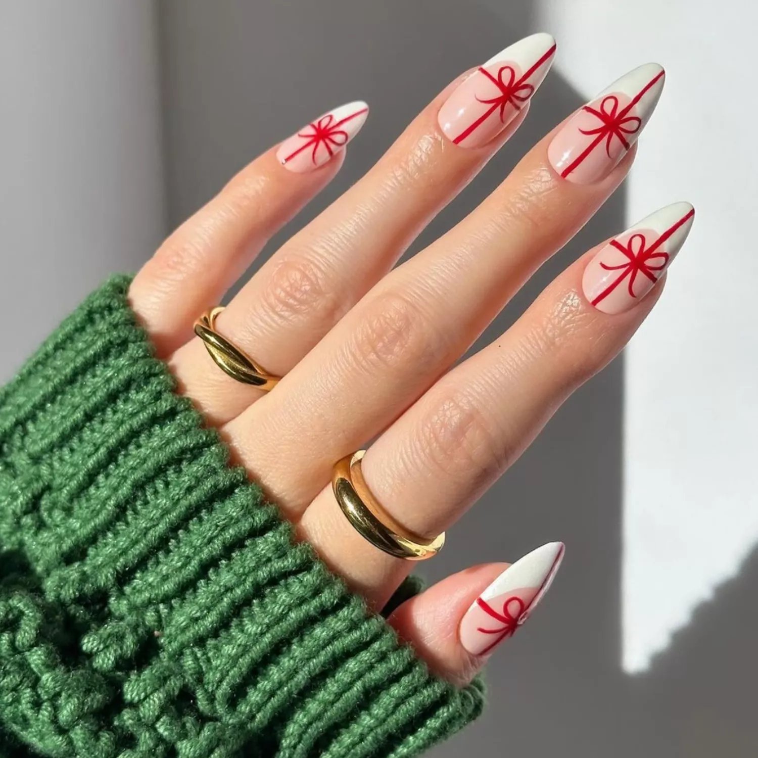 close up of hand showing off fresh manicure, nails with light pink base and white french tip with red ribbon design mimicking shape of present