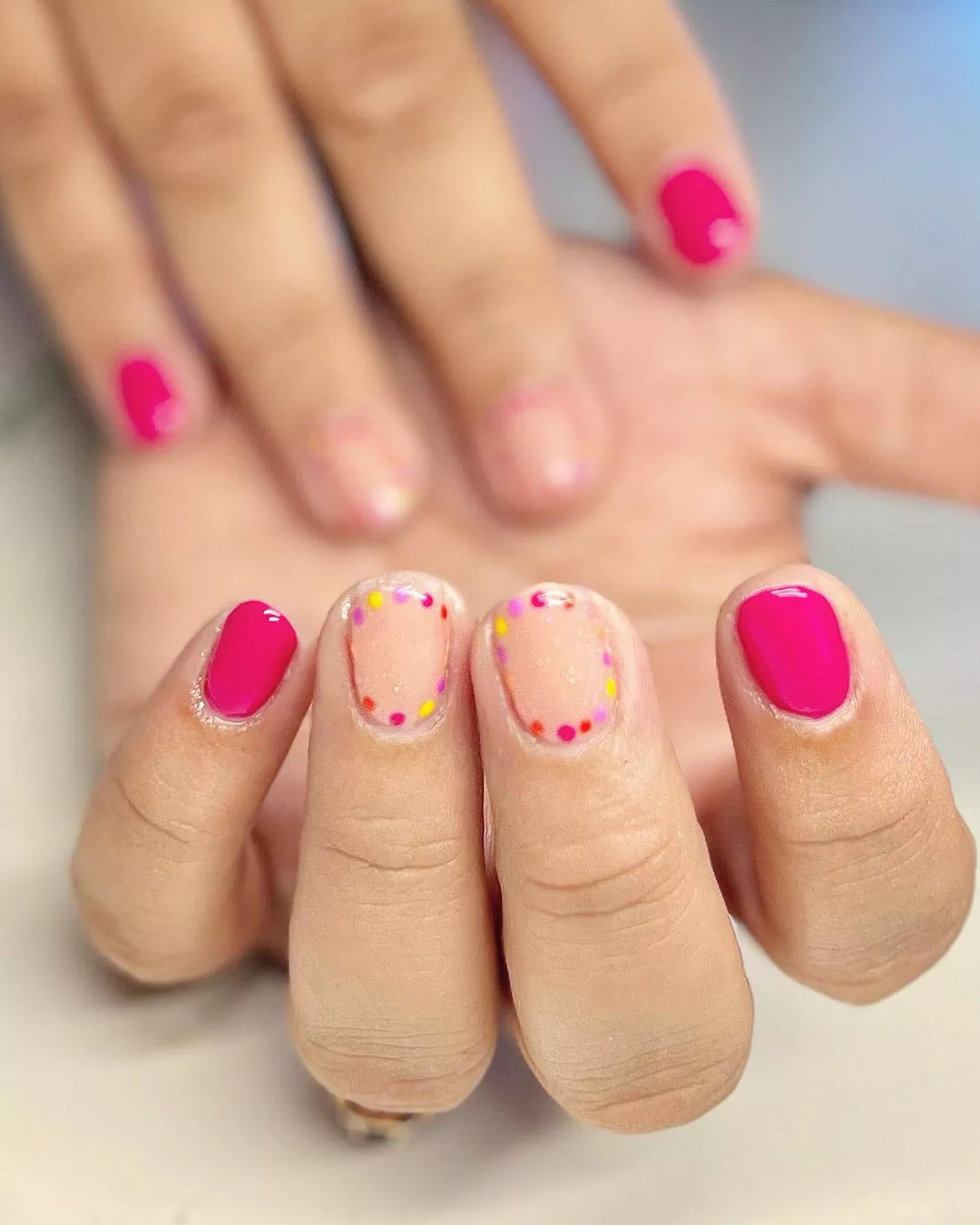 A woman wearing a simple nail design featuring pink and yellow polkadots