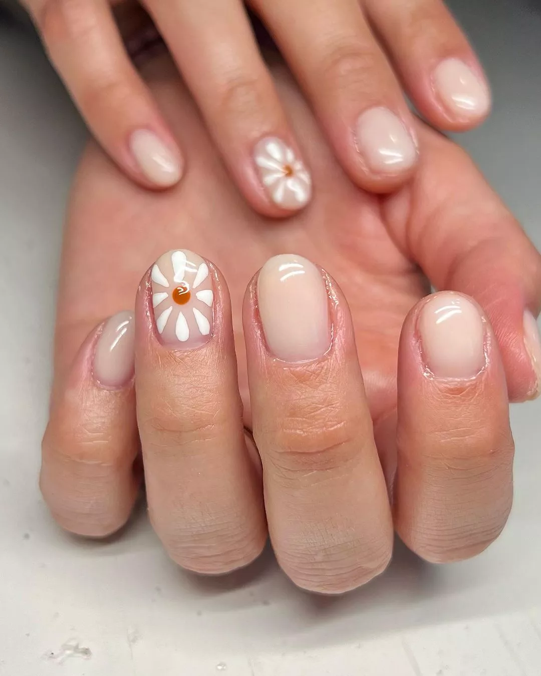 A woman wearing a simple nail design featuring a white flower on each ring finger