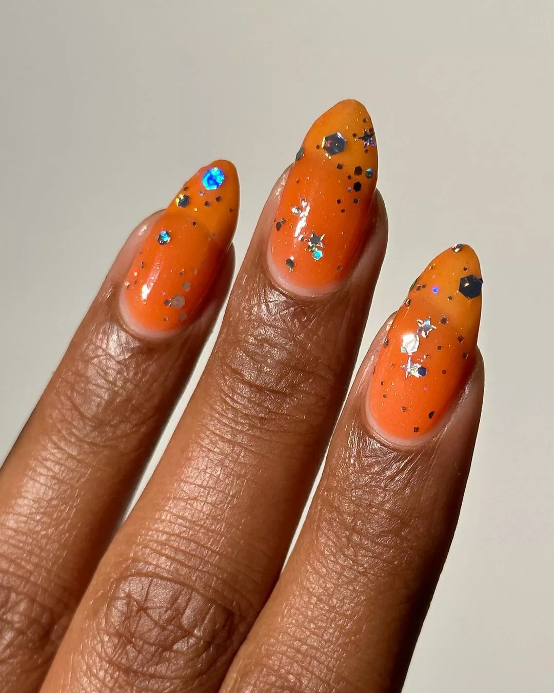 A woman wearing a simple nail design featuring an orange base and glitter topcoat