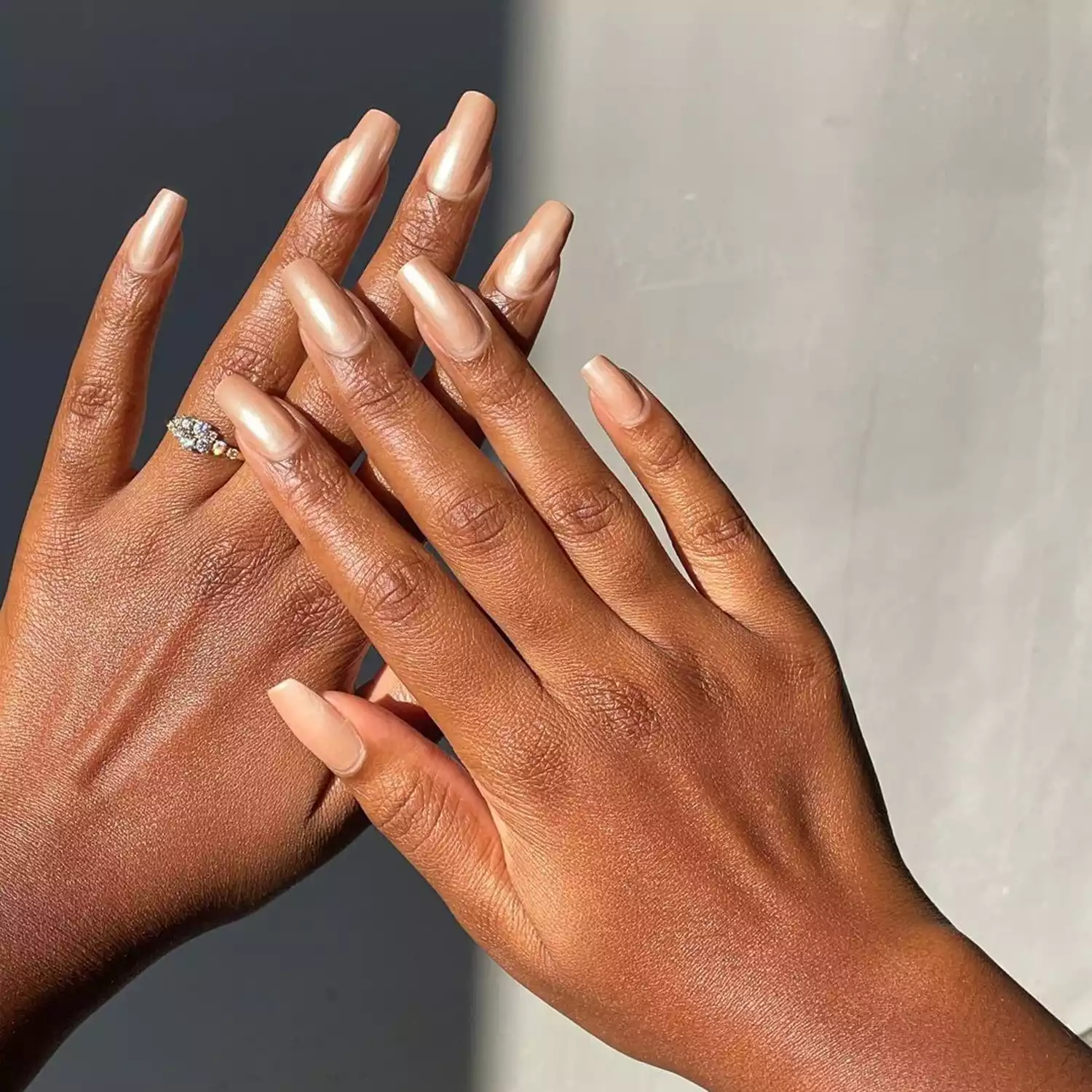 Two hands, one in front of the other, both with a neutral chrome manicure