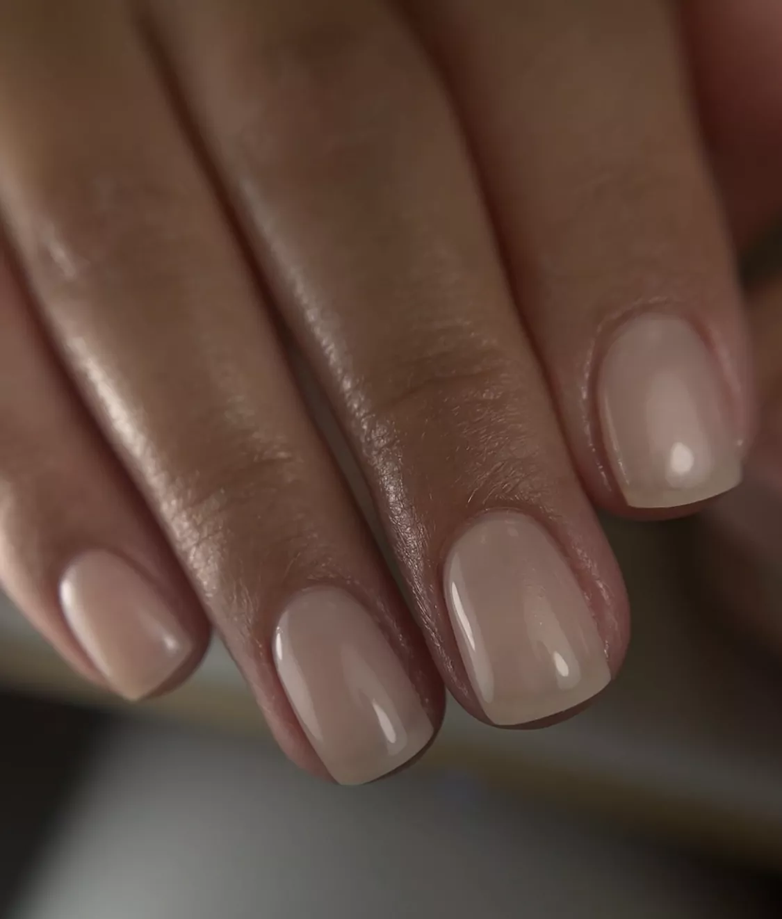 A woman wearing a simple nail design featuring a milky, beige color