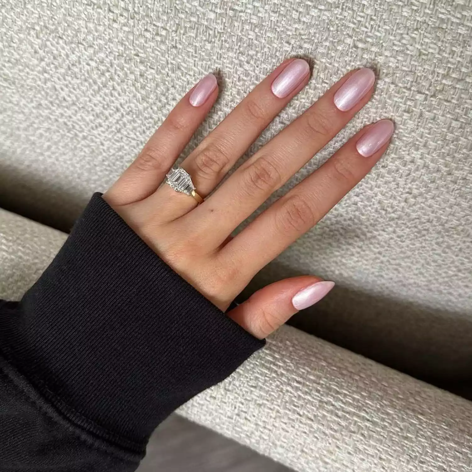 A hand with a pink chrome manicure resting on a piece of furniture