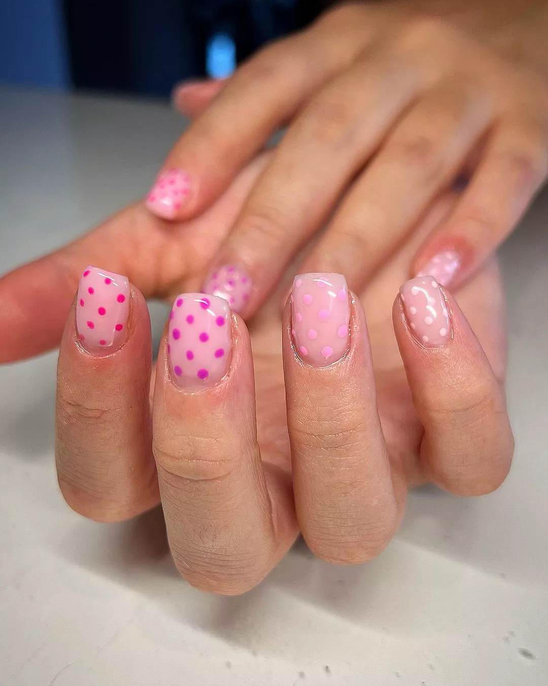 A woman wearing a simple nail design featuring pink polkadots