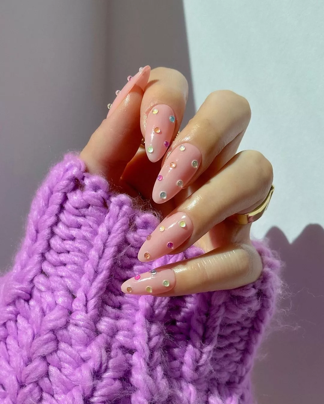 A woman wearing a simple nail design featuring multi-colored crystals