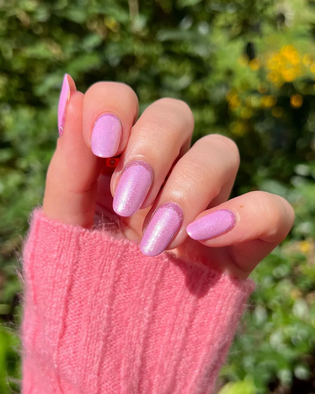 A woman wearing a simple nail design featuring shimmery pink polish