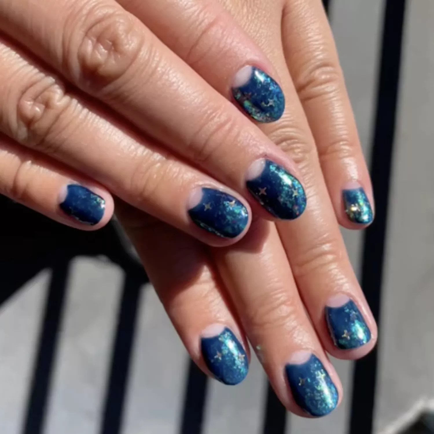 Shimmery blue manicure with negative space half-moons and chrome star nail designs