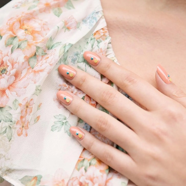 classy peachy pink nails with blue and yellow jewel accents creating a colorful yet simple design