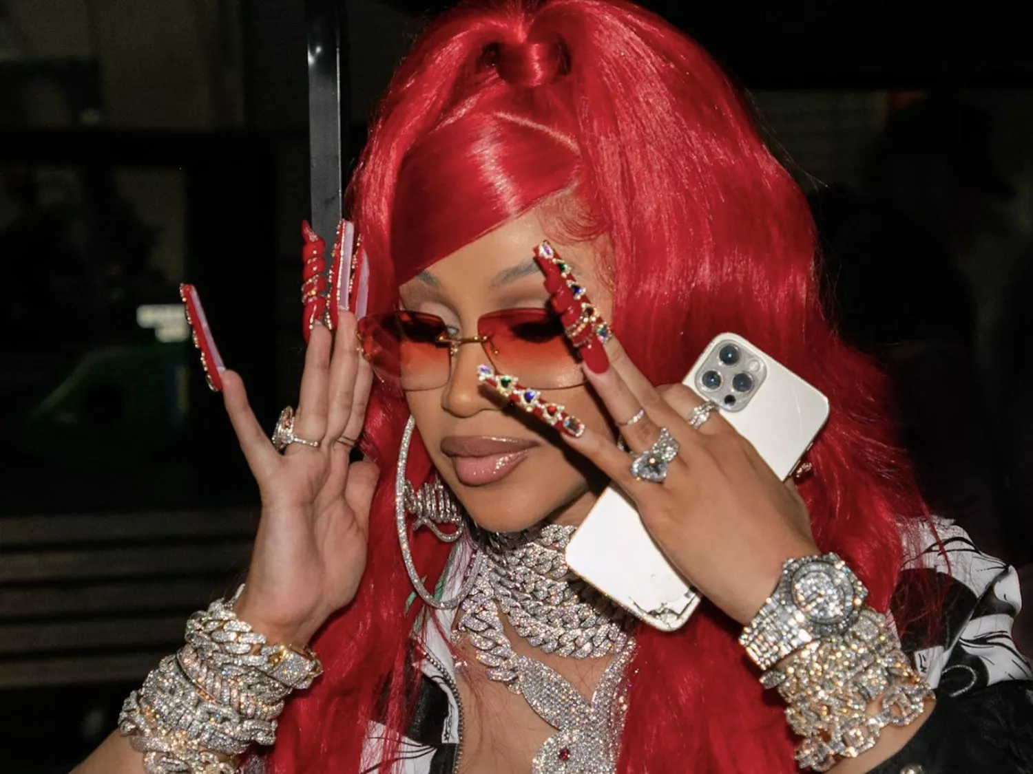 Close up of Cardi B with her hands near her face, featuring long red nails with jewels