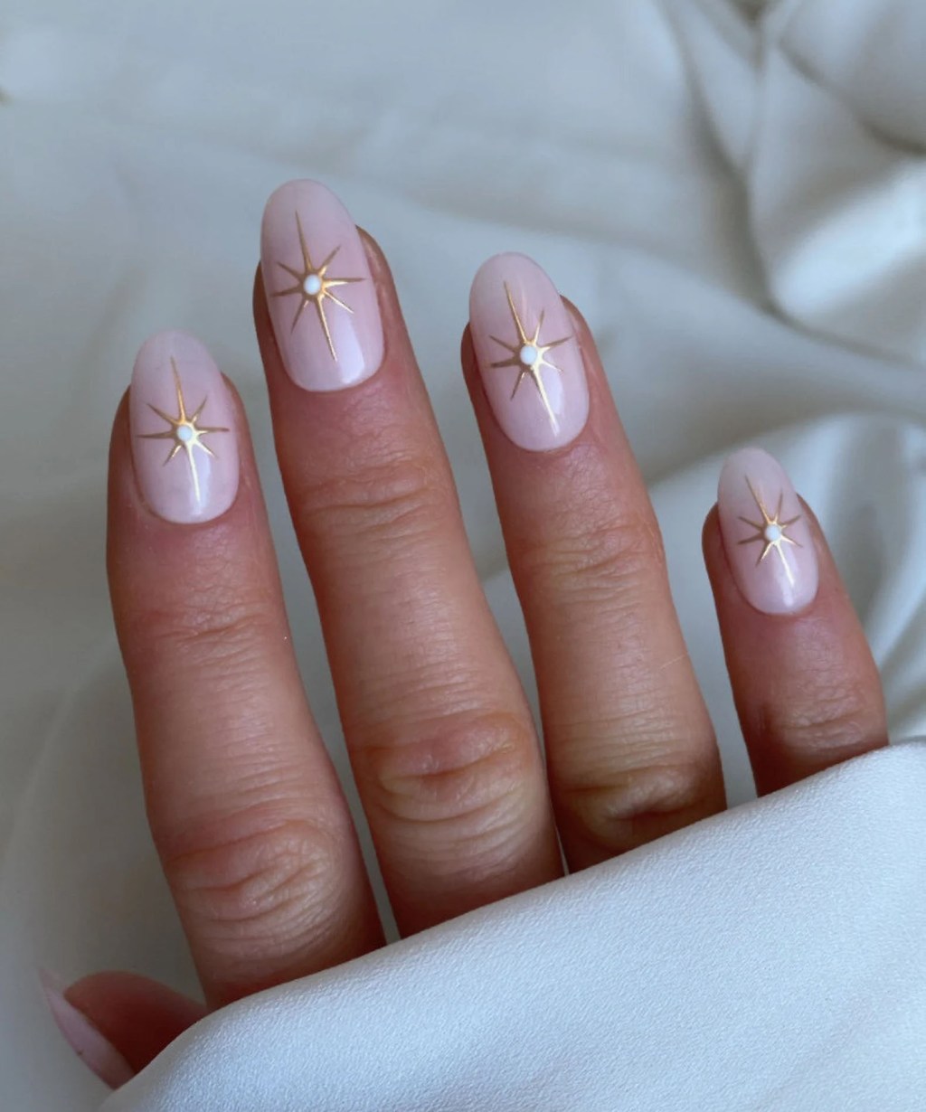 bride showing off her celestial gold sparkle star dotted almond shaped light pink bridal wedding nail designs