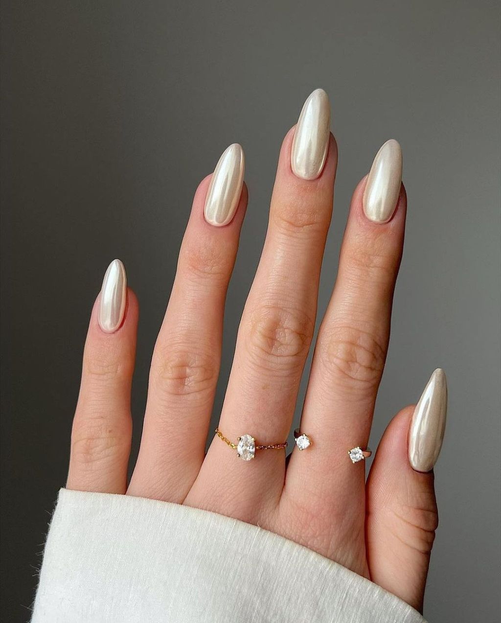 bride wearing classy pearlescent chrome almond shaped wedding nails with a diamond band on her middle and pointer fingers