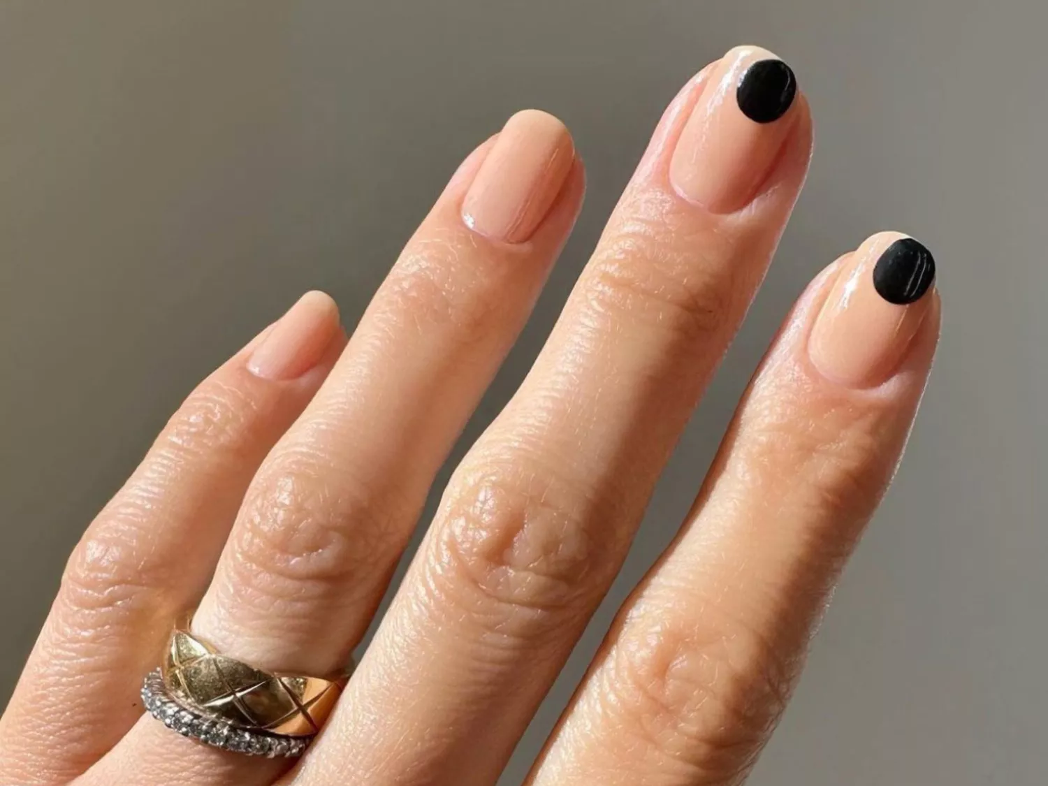 A nude manicure with two black-dot accent nails