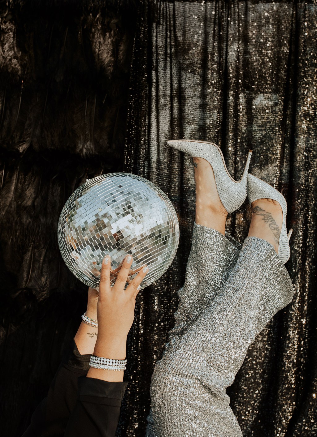 woman holding a disco ball and wearing sequin silver pants and sparkly heels