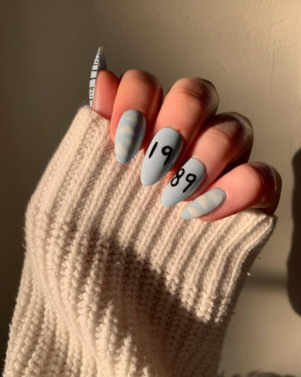 light blue Taylor Swift nails with a cute cloud design inspired by the 1989 album on the Eras Tour and the middle and ring fingers including the date 1989 in black polish