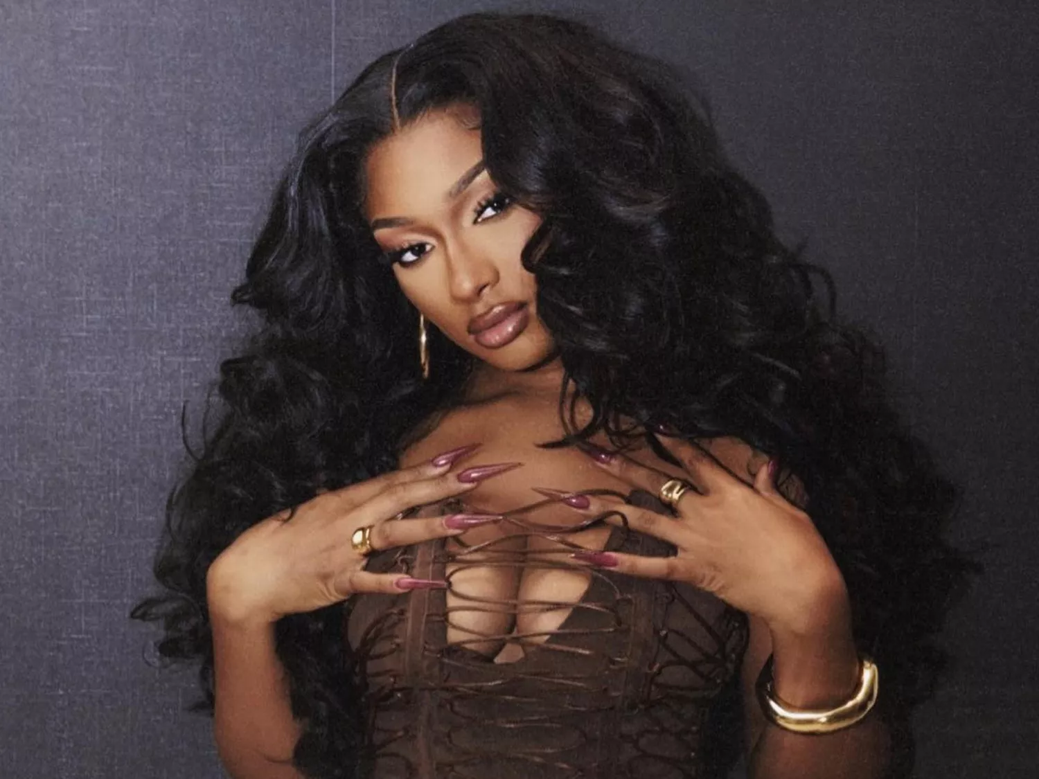 Megan Thee Stallion with a brown corset top, fluffy hair, and reddish-brown nails