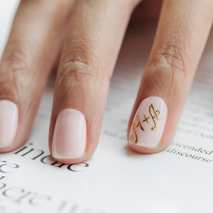 pink wedding nails with gold initials painted on the ring finger