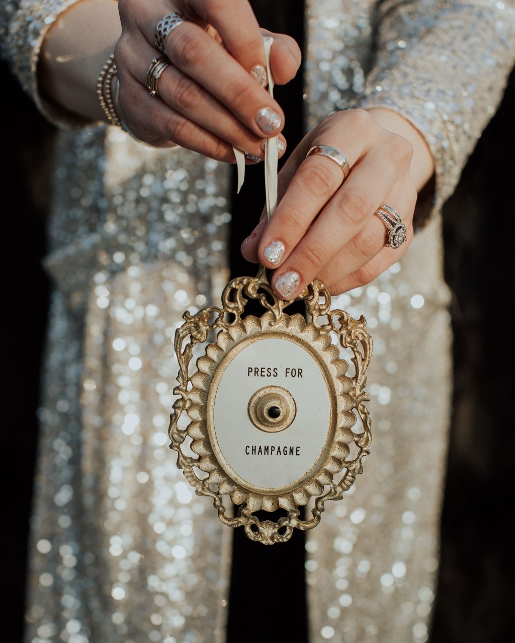 woman short glitter silver new years nails holding a small doorbell that says "press for champagne"