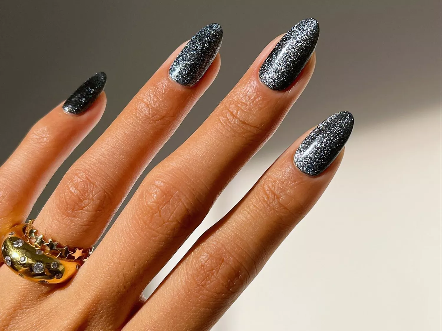 Black and silver glitter manicure with gold layered rings on finger