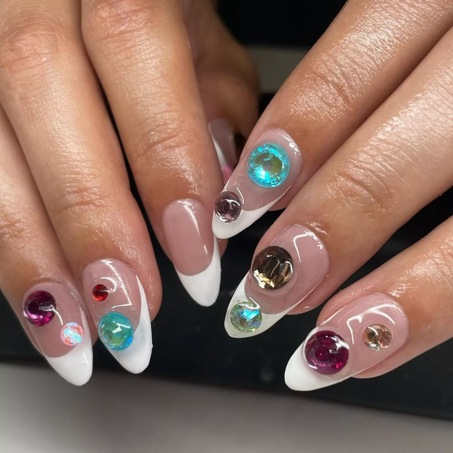 Close-up of manicure with neutral base, white French tips, and colorful 3D gems