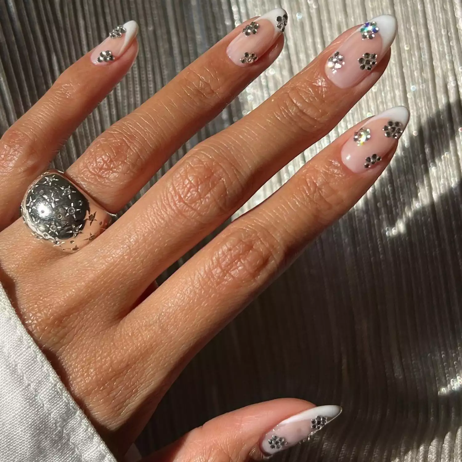 Close-up of manicure with neutral base, white French tips, and mirrored silver flower accents