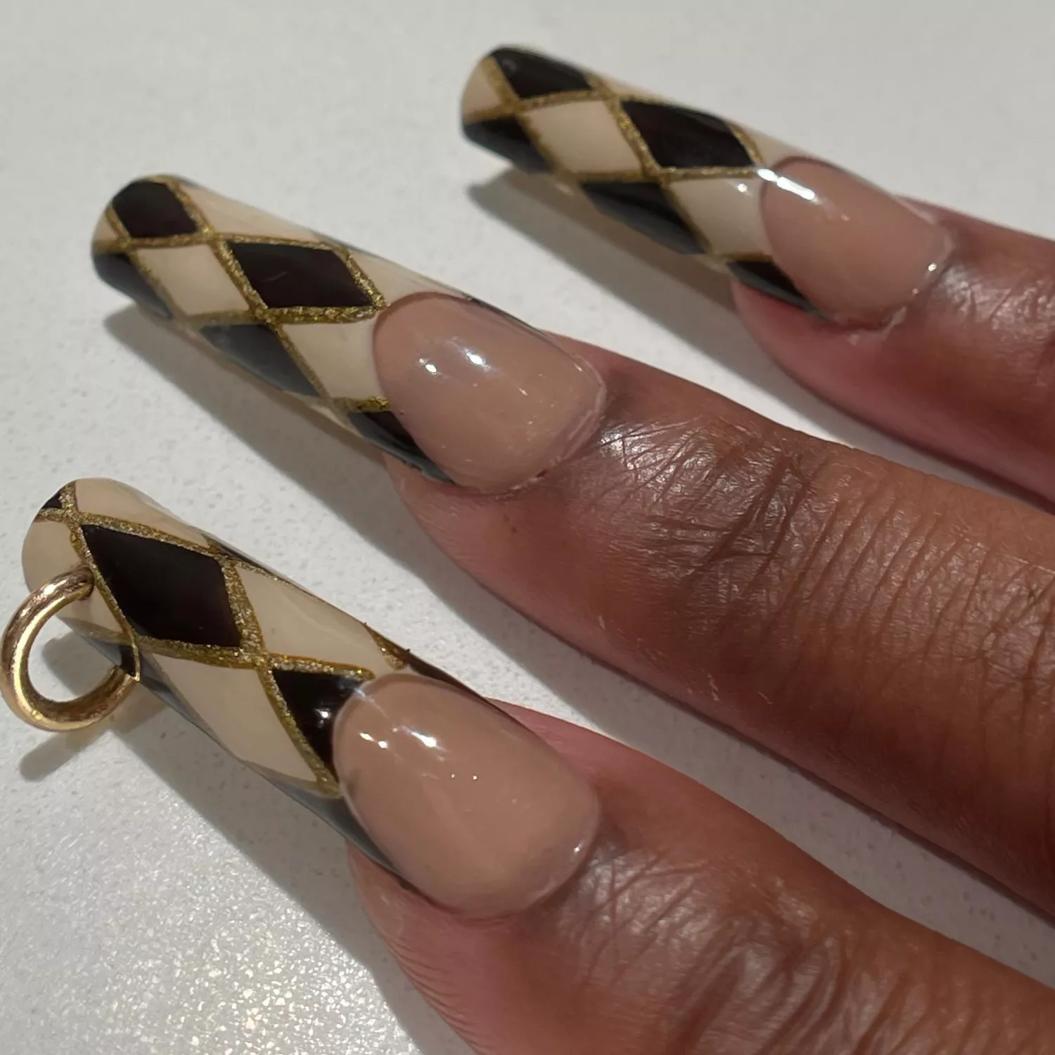 Close-up of manicure with brown, white, and gold art deco diamond design and nail piercing