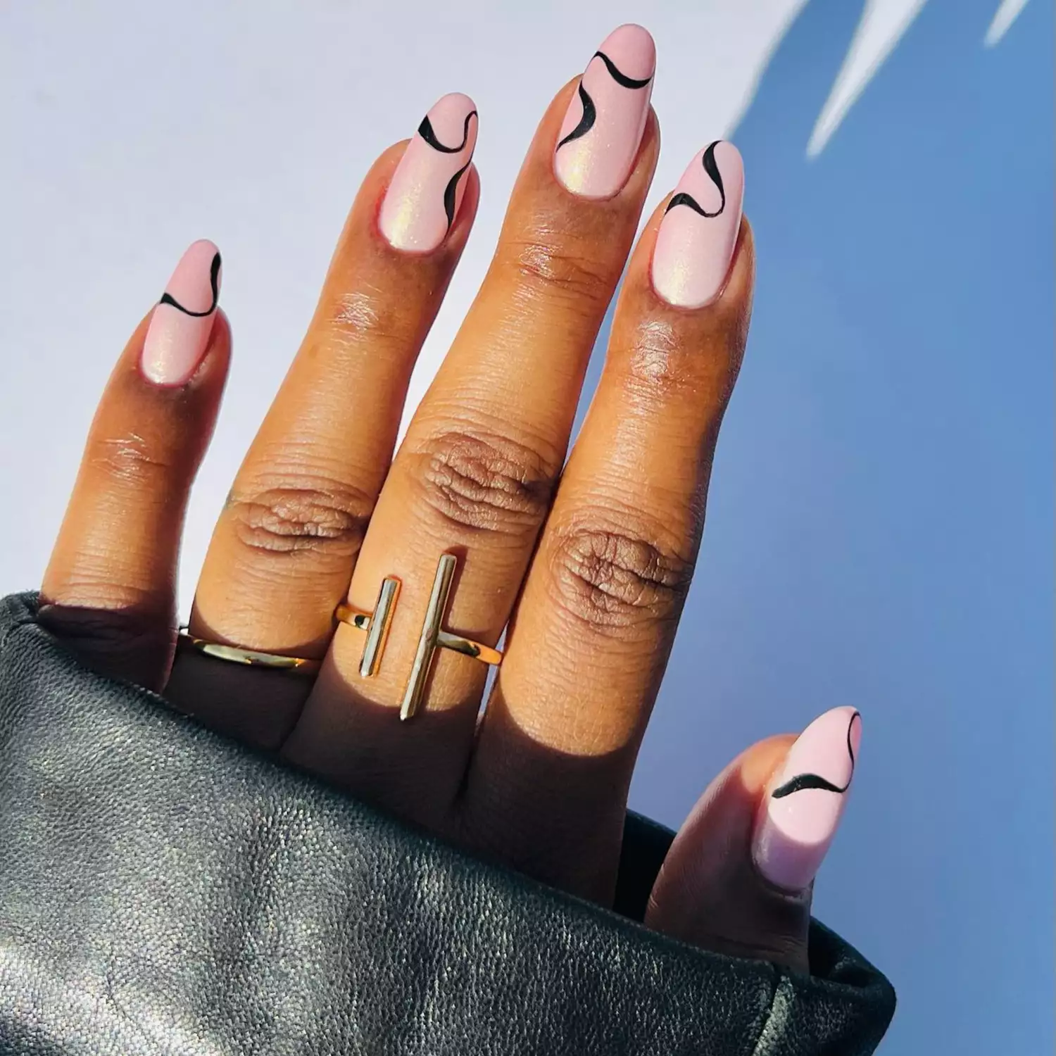 close up of nails with light pink pearly base and black swirls on top