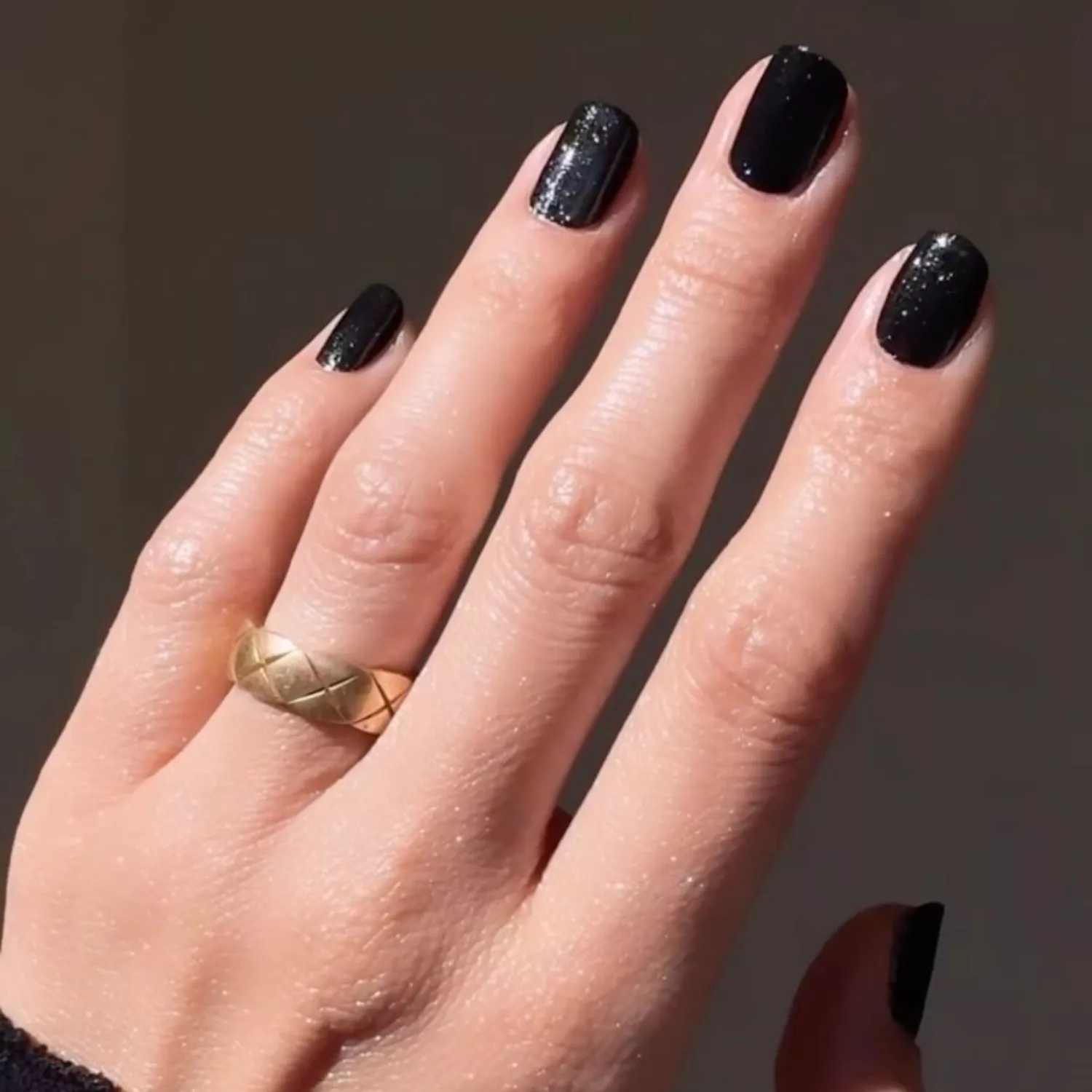 Jet black manicure with glitter detail and gold ring on finger